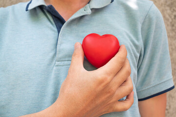 hand holding a red heart to his chest.Health, medicine, cardiology concept.Heart health insurance,...