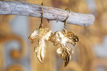 Brass metal earrings in ornamental shape hanging on neutral background - 436327380