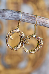 Brass metal earrings in ornamental shape hanging on neutral background