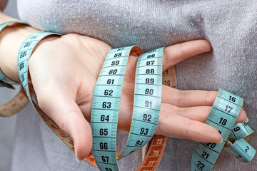 Caucasian woman hand holding the measuring tape with the 90-60-90 centimeters on it. The ideal...