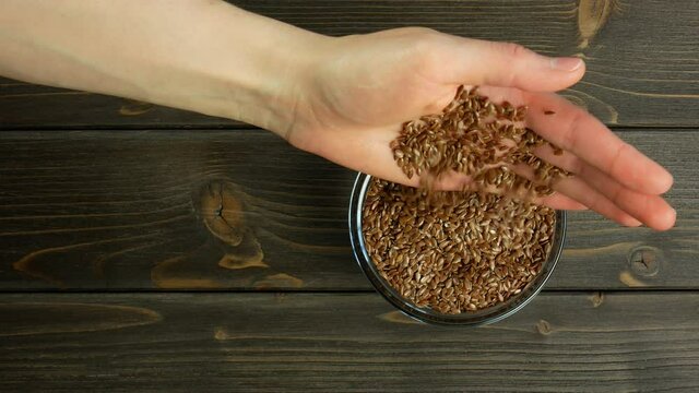 Hand pours flax seeds. Falling flax seeds. Rustic wooden table. Top view, flat lay.