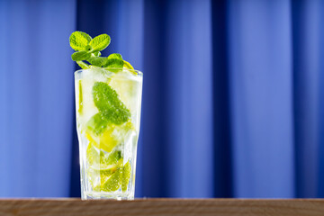 Mojito cocktail on wooden background. Summer mojito cocktail in a tall glass. Refreshing drink with lime, mint and ice. Trendy beverage