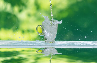 Water splash in glass Select focus blurred background.Drink water pouring in to glass over sunlight and natural green background.Nature conservation concept.