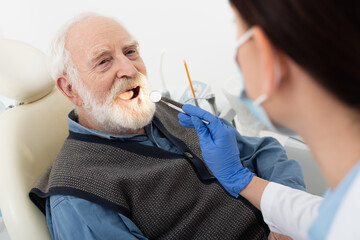 senior man having teeth examination by dentist in latex gloves with mirror in dental chair.