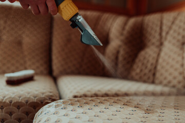 Close-up of housekeeper holding modern washing vacuum cleaner and cleaning dirty sofa with...