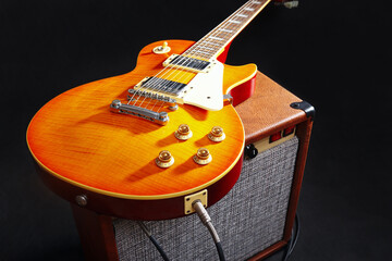 Naklejka premium Brown guitar combo amplifier with honey sunburst guitar on black background.