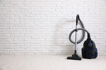 Modern vacuum cleaner near white brick wall indoors, space for text