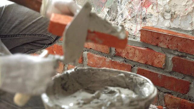 Unrecognizable bricklayer lays red bricks with mortar to make a wall. Rack focus