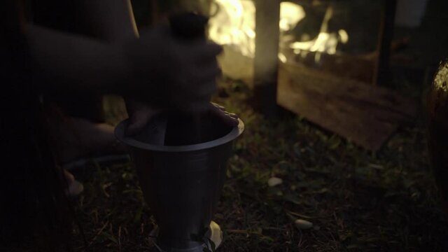 Backlit by fire, cook uses mortar and pestle to mash garlic for chulha