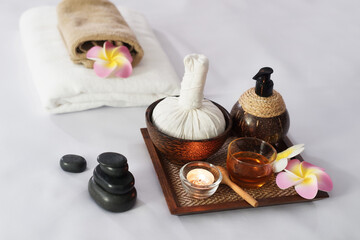 Fototapeta na wymiar Hot compress herbs, Atmosphere candle, honey glass on Herbals tray for therapy massage. Natural black stone and Plumeria flowers decorate on bed at alternative medicine healing spa Center in Thailand.