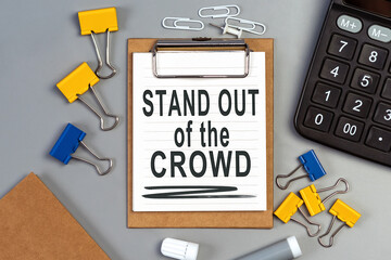 The words Stand out of the crowd written on a white notebook. Work and study concept