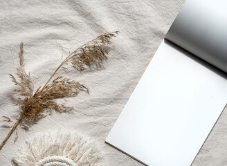 Mockup, block note and pampas grass on off white textile. Simple minimal flat lay on ivory textile with dry earth color reeds. Neutral beige natural materials,. Top view mockup.