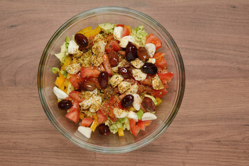 Greek salad with cheese, vegetables and olives in a glass bowl, on a wooden table. Top view close-up