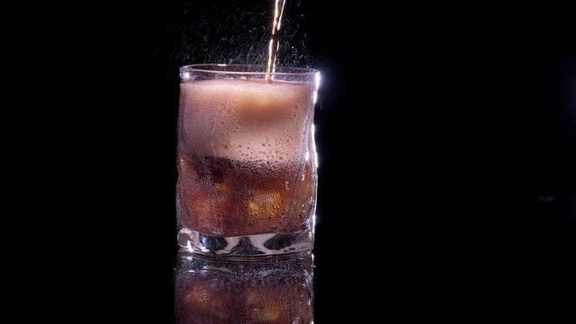 a cola is poured into a glass of ice and lime, on a black background