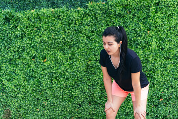 Portrait of young athletic woman resting after jogging. Beautiful woman jogging in the park. Woman runner listening to music while jogging.