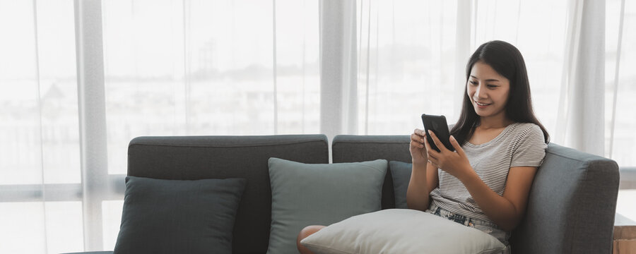 Asian Woman Relax And Using Mobile Phone On Sofa In Living Room At Home