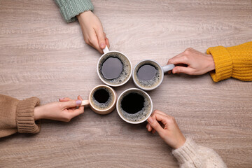 Women with cups of coffee at wooden table, top view