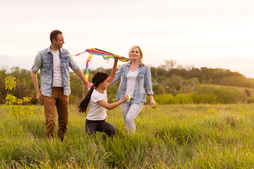 Fototapeta premium Happy family in the park evening light. The lights of a sun. Mom, dad and baby happy walk at sunset. The concept of a happy family