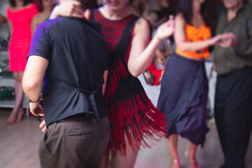 Fototapeta na wymiar Couples dancing traditional latin argentinian dance milonga in the ballroom, tango salsa bachata kizomba lesson in the red, purple and violet lights, dance festival