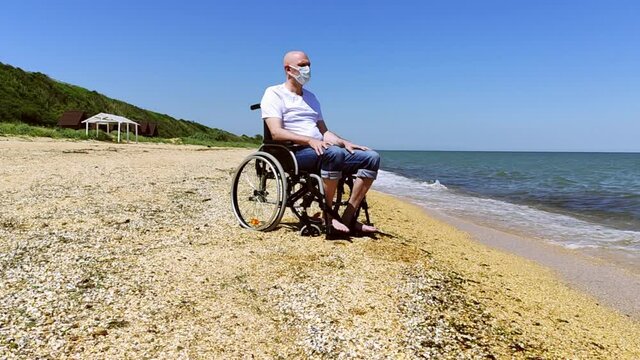 Man in medical mask and wheelchair by the sea. High quality 4k footage