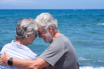 Back view of senior couple in love sitting on the beach looking each other. Two retired enjoying summer vacation and freedom