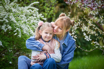 Fototapeta premium Handsome blonde mother and child daughter together in a blossom park