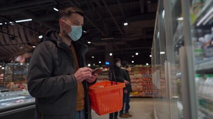 Man chooses groceries in store, walks with shopping basket, buys essential goods during quarantine in supermarket, wears protective medical mask. New normal, covid 19 and purchases. No mask no entry