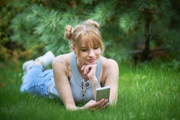 Fototapeta premium Portrait of smiling young woman with smart phone lying on grassy field at public park