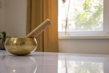 There is a singing bowl on the table with a resonator (darshan, stick) inside. An oriental musical instrument that vibrates and produces very pleasant and useful sounds for the hearing and body. - obrazy, fototapety, plakaty