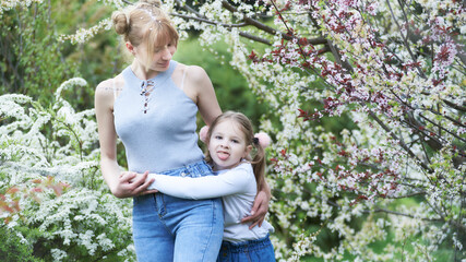 Fototapeta premium Beautiful blonde mother and child daughter together in a Blossom park, sticking out tongue
