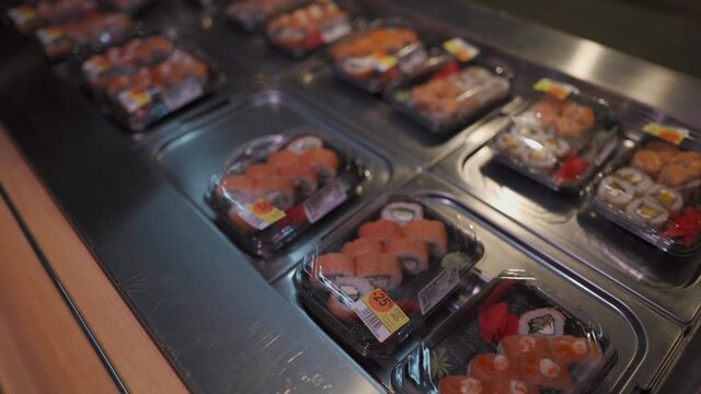 Caucasian man wearing protective mask on his face chooses set of sushi in box to go in supermarket during quarantine and coronavirus epidemic. Japanese food for take away. Healthy food, lunch box