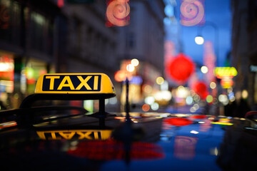 Close up of illuminated taxi sign reflecting on taxicab roof, neon light in background, night scene.