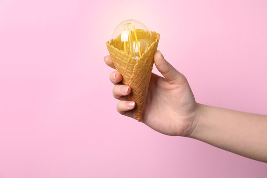 Woman holding waffle ice cream cone with light bulb on pink background, closeup