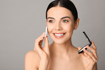 Beautiful young woman applying face powder with puff applicator on grey background - obrazy, fototapety, plakaty
