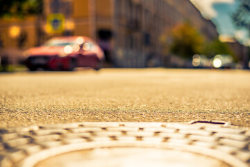 Clear day in the big city, a quiet street with trees and cars. View from the hatch on the pavement level