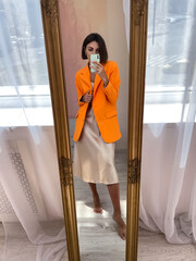 Fit tanned woman in romantic beige silk dress and orange blazer at home take photo selfie on phone...