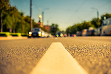 Clear day in the big city, a city street near the park with headlights of the approaching cars. View from the level of the dividing line