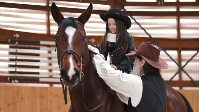 Senior man assisting granddaughter horseback riding in ranch
