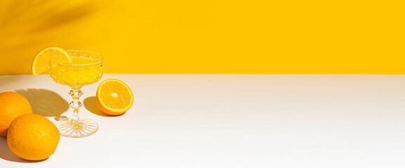 Glass of cocktail or orange juice under the shade of a palm tree and sunlight. Summer concept, vacation at sea. Banner