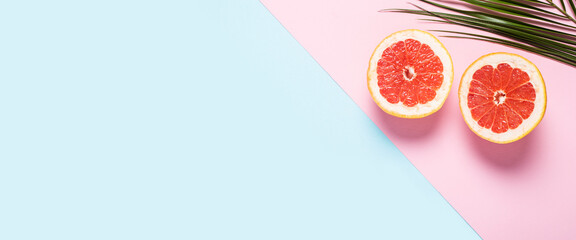 Sliced grapefruit and palm branch on a pink and blue background. Banner. Flat lay, top view