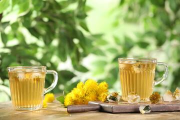 Delicious fresh tea, dandelion flowers and ice cubes on wooden table against blurred background - Powered by Adobe