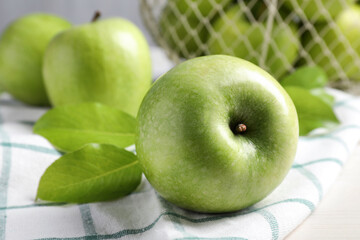 Fresh ripe green apples with leaves and napkin on table, closeup