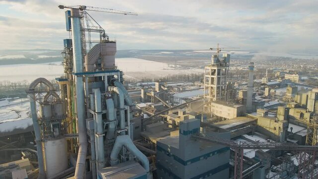 Aerial view of cement plant with high factory structure and tower crane at industrial production area at sunset.