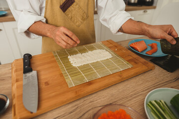 Chef making perfect sushi with bamboo mat. Close up wide angle male hands cooking on kitchen sushi rolls with salmon fish