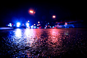 Naklejka premium Night city after rain, approaching car headlights shine. View from a wide angle at the level of the asphalt
