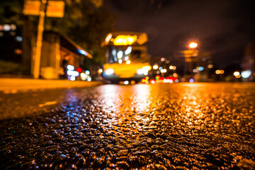 Night city after rain, the glowing lights of approaching bus. View from a wide angle at the level of the asphalt