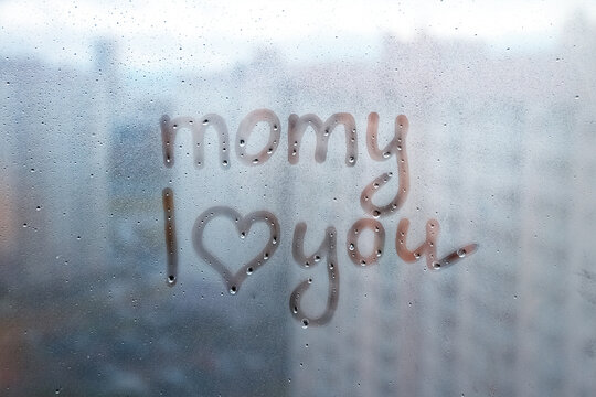 Foggy glass on window with written finger word momy i love you with heart shape on blue overcast wet window