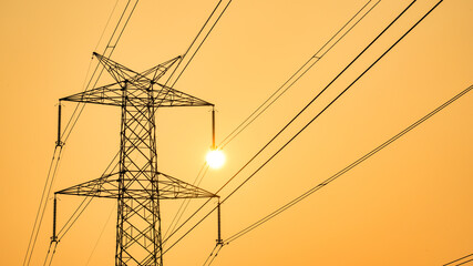 High power electricity pole silhouetted against the orange sky at dusk, Electric pole in India,...