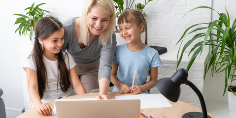 Beautiful young mother helping her daughters with homework.