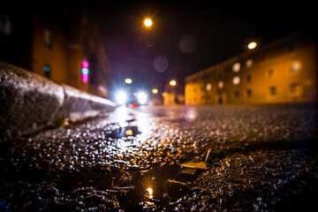 Rainy autumn night in the city, the glowing lights of approaching car. Wide angle view of the level of the curb on the road